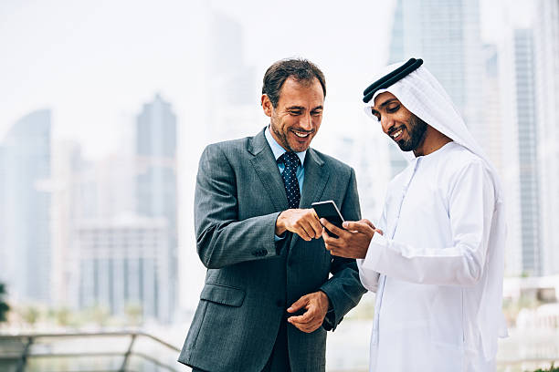 Emirati and Western businessmen checking content on smart phone. The man in white clothes is holding black smart phone.